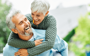 CDs-IRAs-712x446 – Chemung Canal Trust Company  A woman is getting a piggy back ride from her husband. They are both smiling.