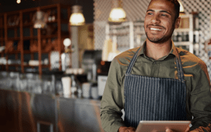 A man is standing in a cafe, wearing an apron