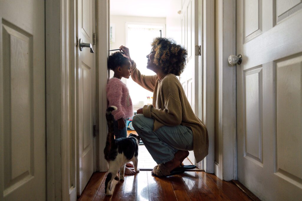 Mother measuring daughters height and marking on wall at home – Chemung Canal Trust Company  African American woman squatting down to measure daughter against door frame