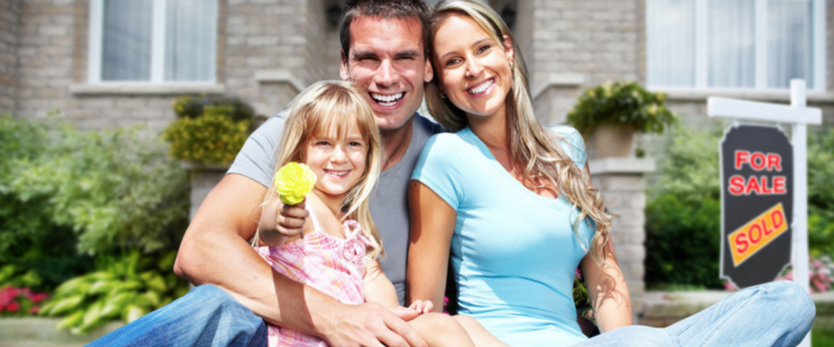 Photo of a mom, dad, and their child seated outside of their house, smiling
