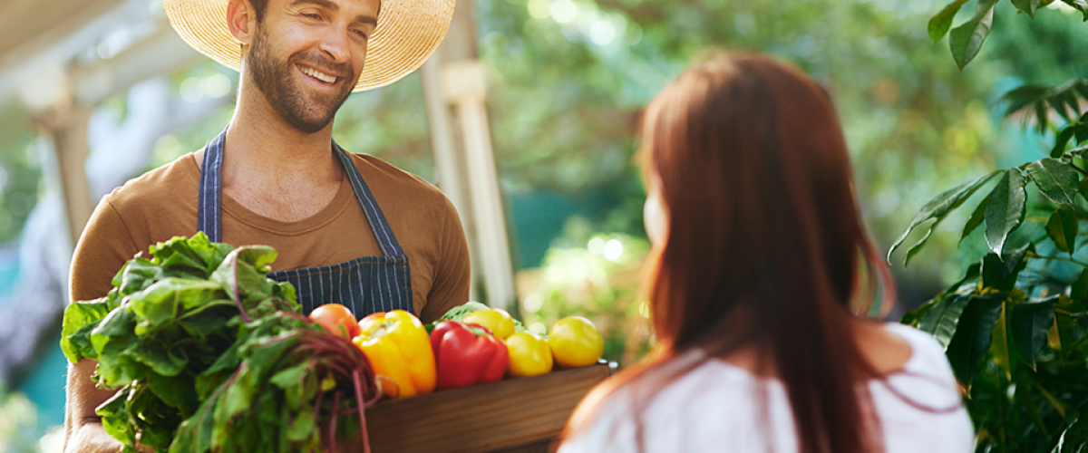 A man in an apron hands a woman a box with fresh produce