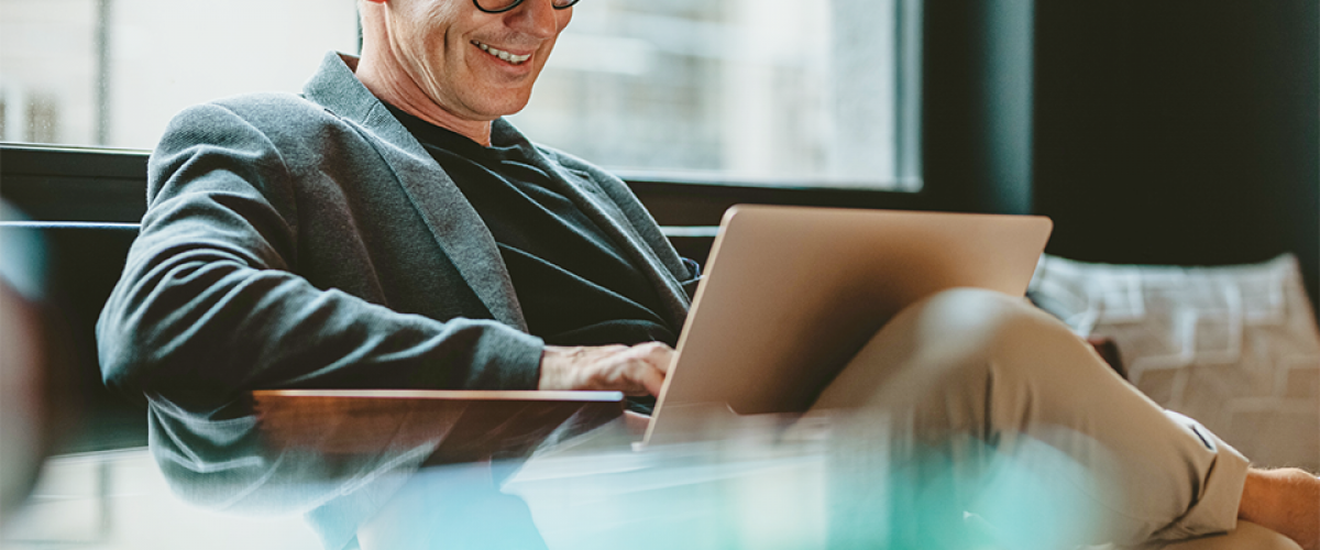 Image of a business man sitting with a laptop computer on his lap. He is working and smiling.