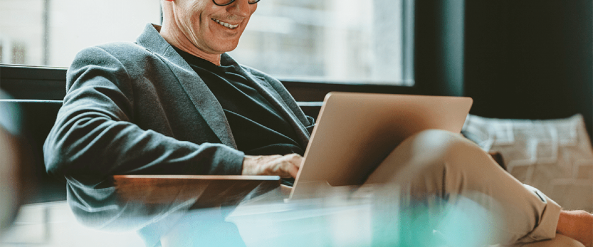 Image of a business man sitting with a laptop computer on his lap. He is working and smiling.
