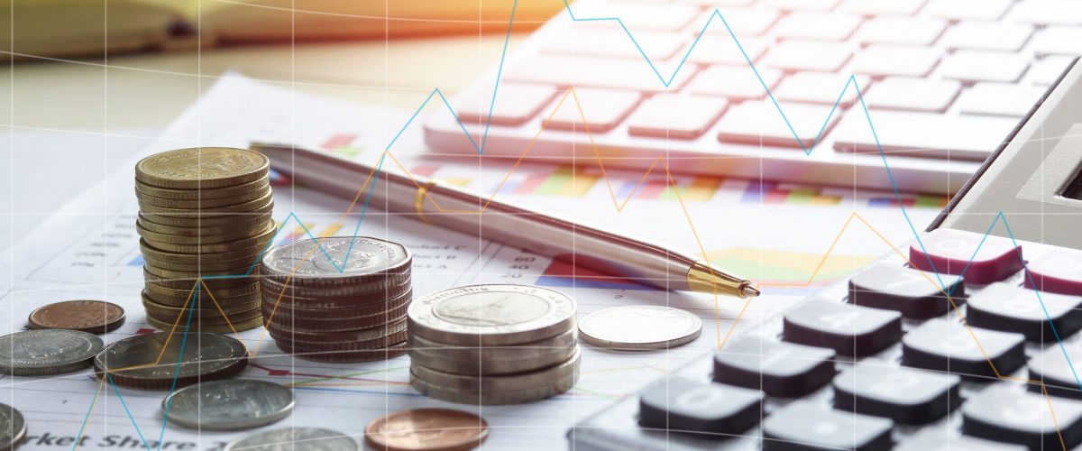 Stacked coins, a calculator, and financial charts on a desk illustrating budgeting and finance precision.